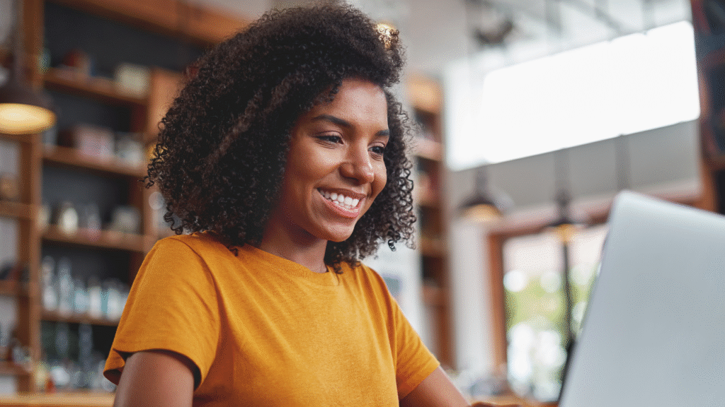 10 Important Steps to Confidently Quit Your Job to Become a Transaction Coordinator 1 Woman smiling while working on a laptop in a café-style workspace while planning her transition into a remote business career.
