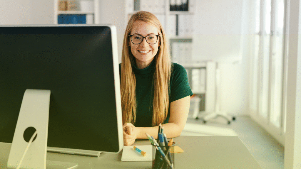 How to Transition from Admin Assistant to Transaction Coordinator 1 woman sitting in front of a desktop computer, smiling.