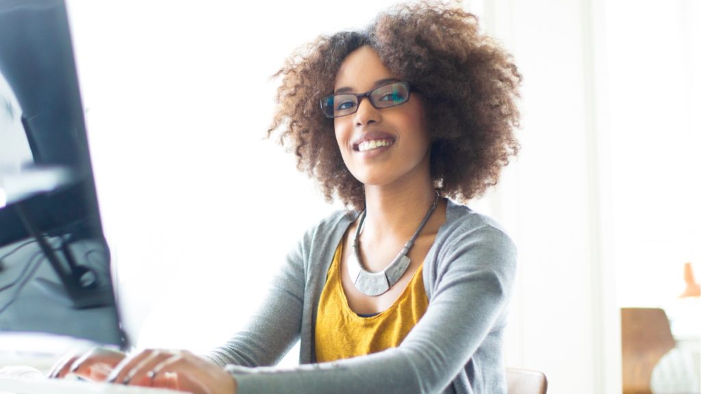 Why Boundaries Make You a Better Transaction Coordinator 1 Woman wearing glasses working at a computer with a confident smile, representing a Transaction Coordinator building professional boundaries through systems and clear client expectations.