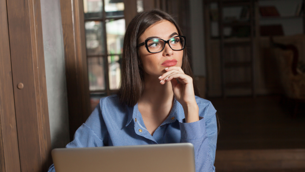 Why Some Realtors Resist Transaction Coordinators 1 Young woman working on a laptop while thoughtfully looking away, representing a Transaction Coordinator wondering why some Realtors resist transactions coordinators